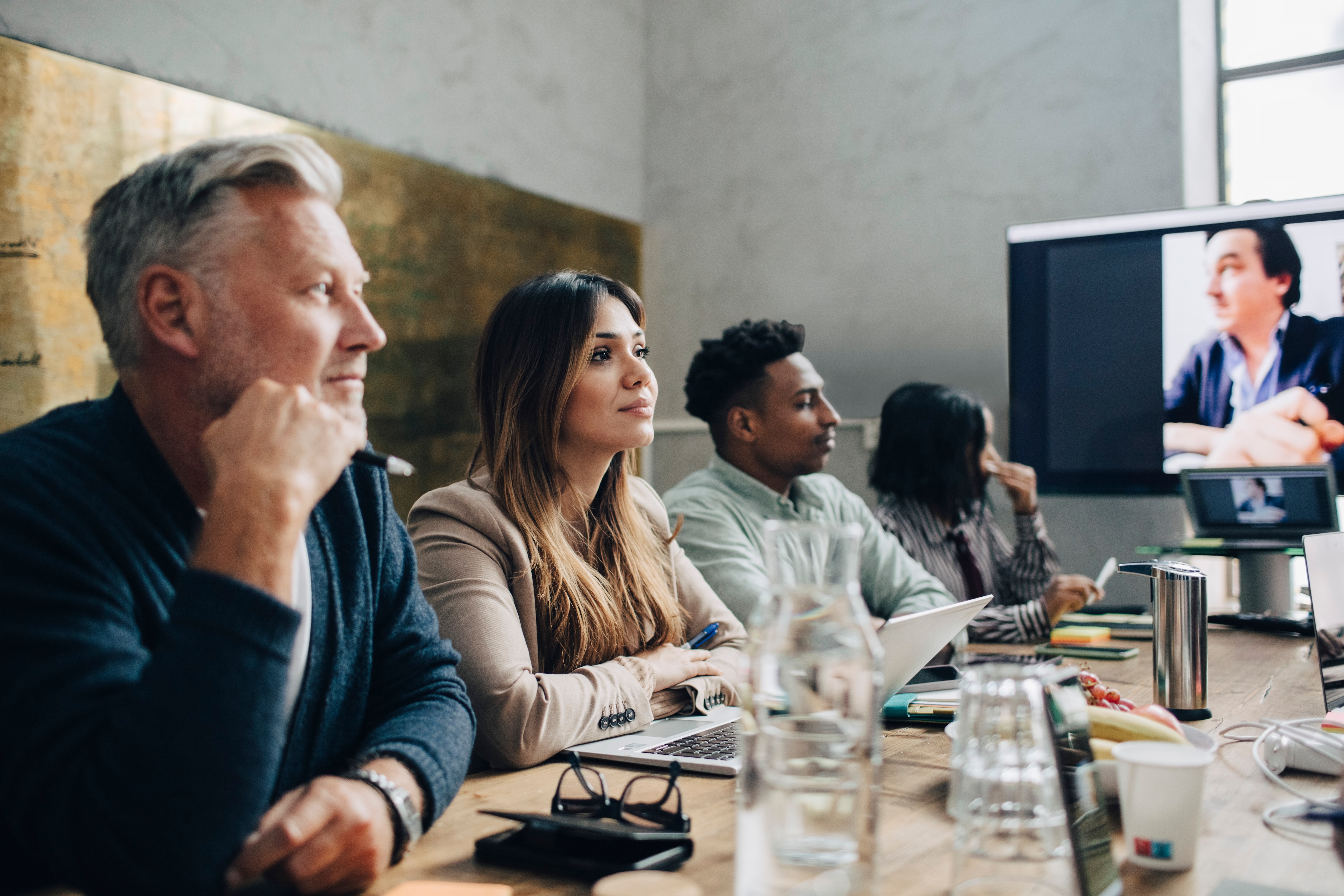 A group of businessmen and businesswomen sitting at a conference table listening to a presenter