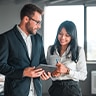 Man and woman in office setting looking at a tablet.