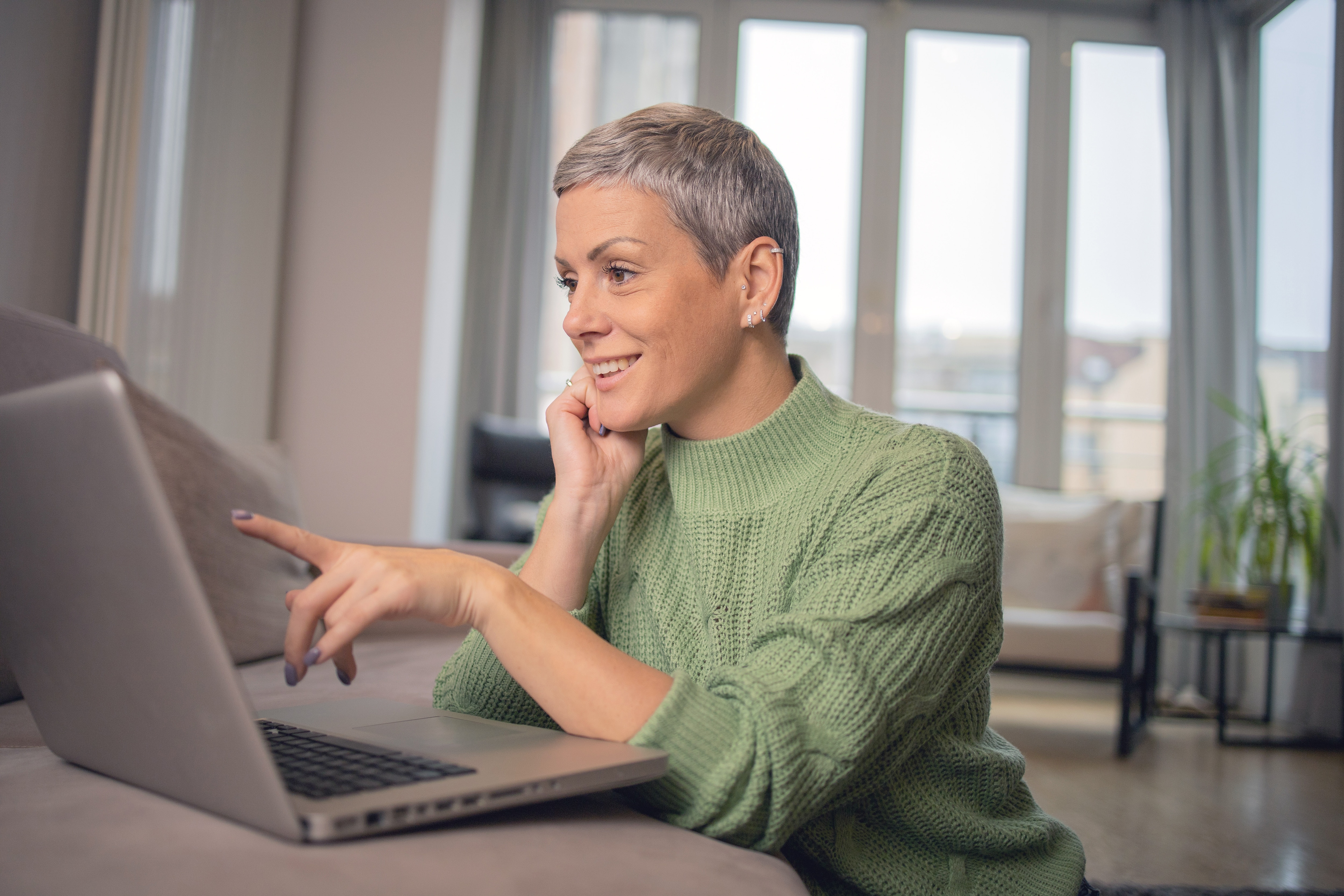 Woman in a green sweater sitting at a table pointing at her laptop