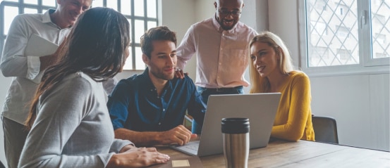 Group of coworkers looking at a seated coworkers laptop