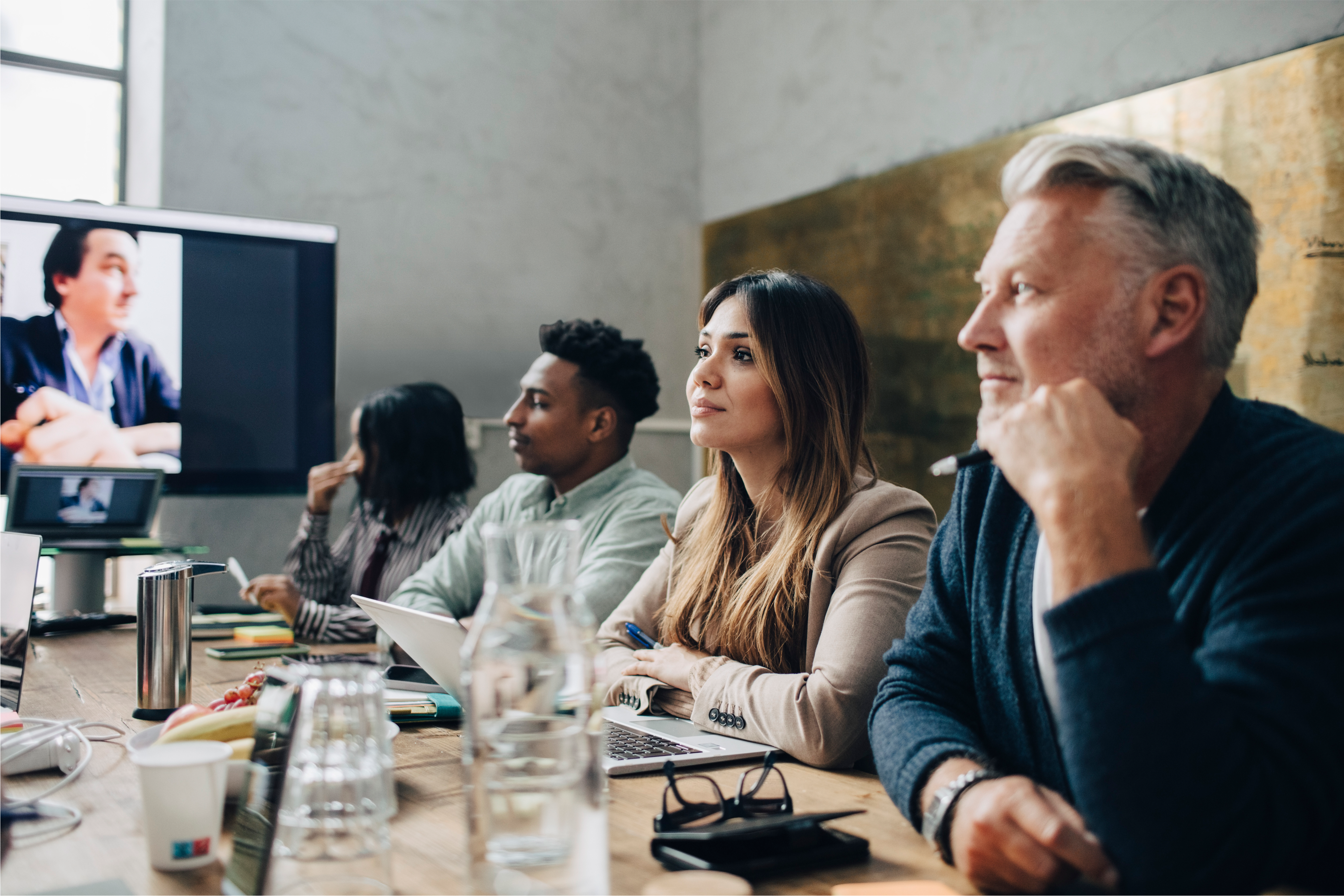 Group of four employees sitting at a wooden table listening to a virtual speaker