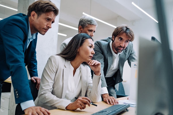 Group of co-workers leaning over a desktop computer looking at the screen