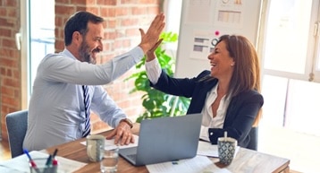 A businessman and businesswoman sitting at a table giving each other a high-five