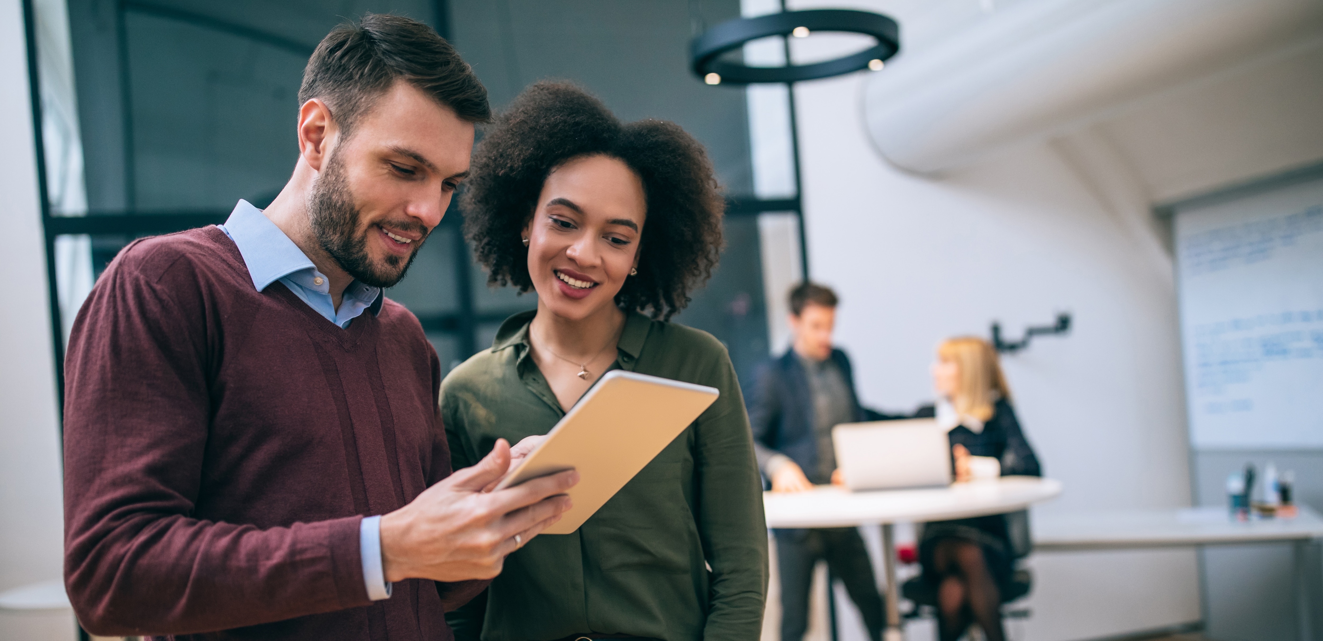 Male in burgundy long sleeve top discussing work with a woman in a green long sleeve top in the office