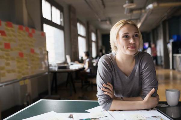 Woman sitting at a table in front of a board full of sticky notes