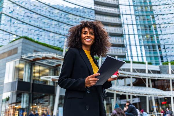 Woman with folder standing in front of glass high rise