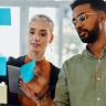 A male and female sorting through sticky notes on a wall in an office
