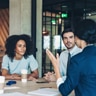 A group of coworkers sitting around a table listening to another coworker speak