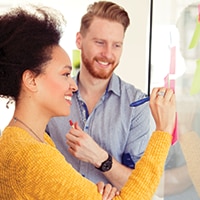 Woman writing on whiteboard while coworker looks on